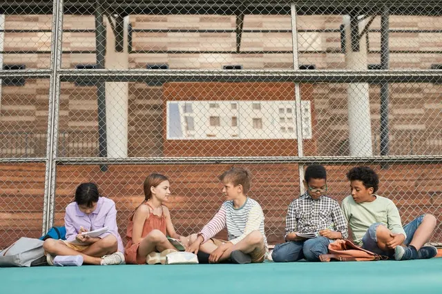 Crianças lendo sentadas no chão de uma quadra escolar