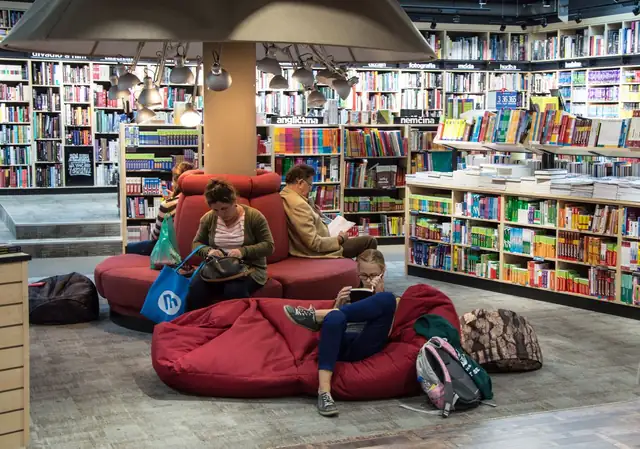Leitores sentados em pufes vermelhos entre estantes de livros
